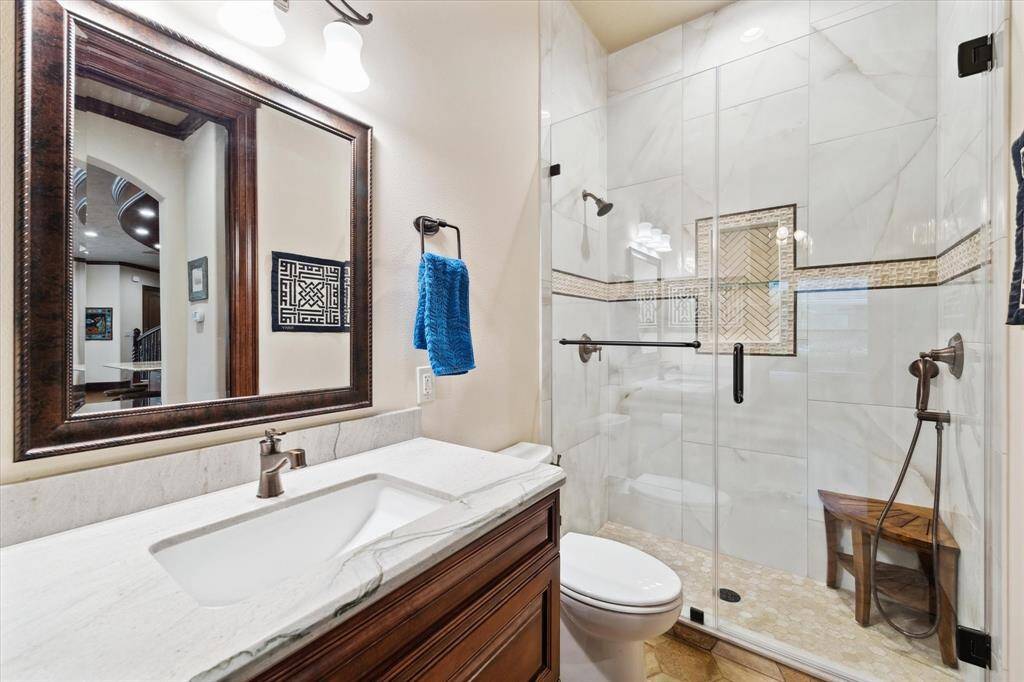 This ensuite bathroom for the secondary bedroom on the first floor features a modern design with a large glass-enclosed shower, elegant marble tiles, and a stylish vanity. The room is well-lit, offering a clean and fresh ambiance.