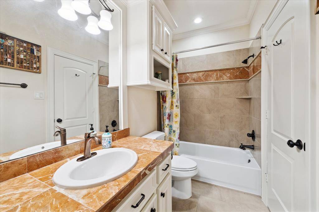 This is a second floor bathroom that features a clean, classic design with a granite countertop, single sink, and modern fixtures. It includes a bathtub with a tiled shower area, built-in shelving, and ample lighting.