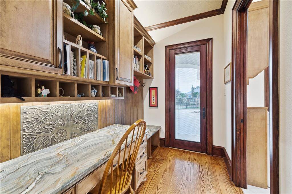 This photo showcases a cozy home office nook or homework area with custom wooden cabinetry and ample shelving. A decorative backsplash adds character above the granite desk. The space is brightened by a glass door leading to the outside, providing natural light.