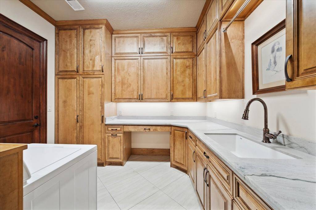 This photo showcases the laundry room with ample wooden cabinetry for storage, a built-in workspace, and a large sink. The room features a warm, natural wood finish and a modern faucet, making it both functional and stylish.