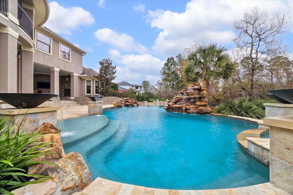 This stunning home features a luxurious outdoor pool with a waterfall, surrounded by lush landscaping and a spacious patio area perfect for relaxation and entertaining.