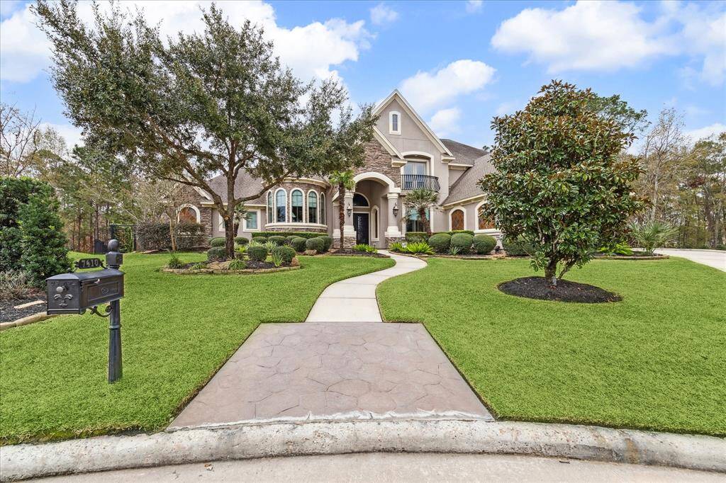 This stunning home features a grand entrance with a well-manicured lawn, mature trees, and elegant landscaping. The exterior boasts a mix of stone and stucco, with large arched windows and a welcoming walkway leading to the front door. Perfect for buyers seeking luxury and curb appeal.