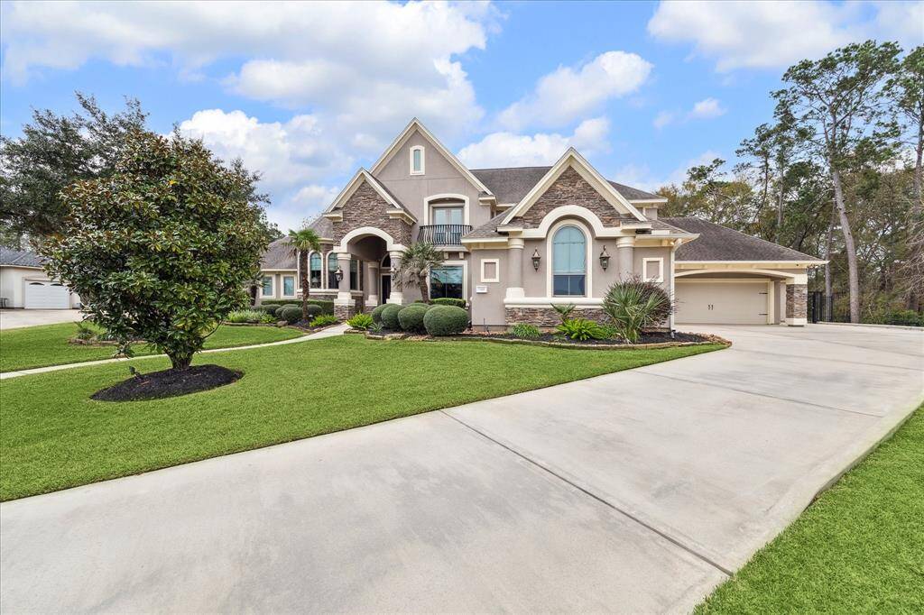 This beautiful two-story home features a stone and stucco exterior, with a well-maintained lawn and elegant landscaping. It has a spacious driveway leading to 2 separate 2-car garages offering 4 car areas. The inviting entrance includes a covered porch with decorative pillars.