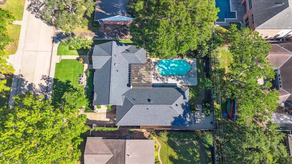 This aerial view showcases a spacious home surrounded by lush greenery. The backyard features a large swimming pool and patio area, offering ample outdoor living space. The property is situated in a neighborhood with tree-lined streets, providing a serene and private setting.