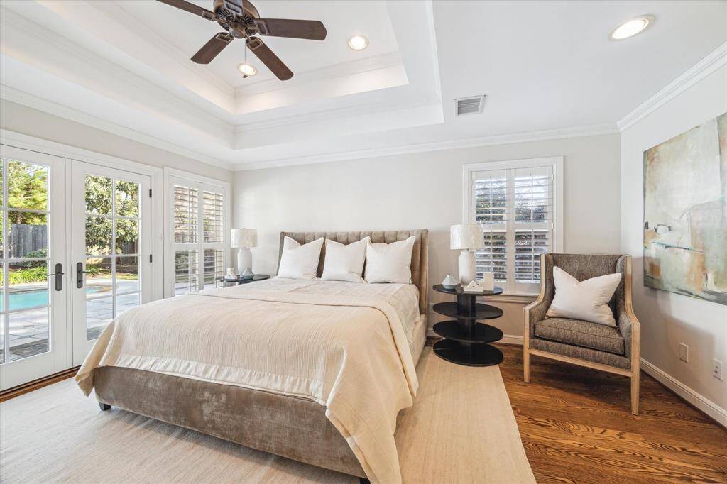 This large primary bedroom features abundant light that floods through French doors and windows with plantation shutters. The room is accented by a ceiling fan and recessed lighting, with views of a serene backyard and pool.