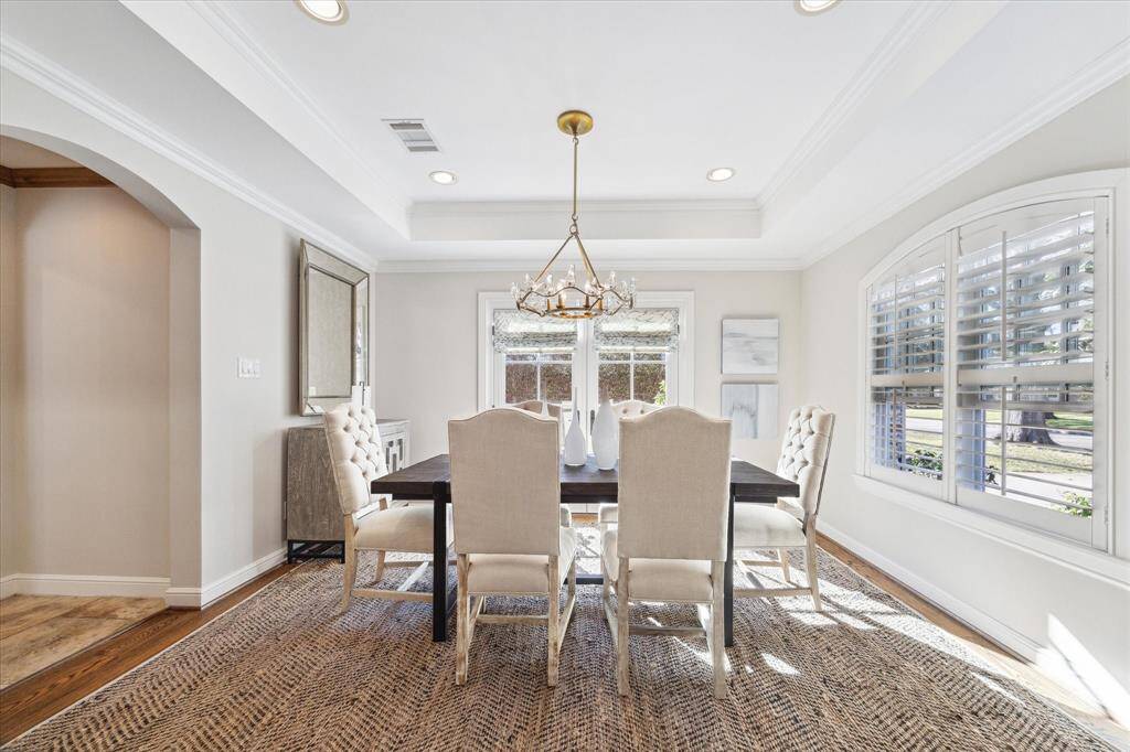 This elegant dining room features a large windows with plantation shutters and double french doors, allowing natural light to brighten the space.