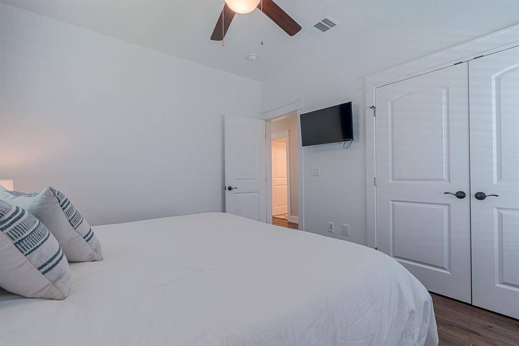 Primary bedroom with ceiling fan, wood floors and mounted TV