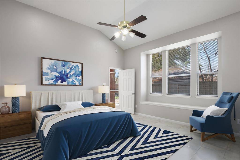 This spacious first floor Primary bedroom features a vaulted ceiling, large windows for natural light, modern decor with a blue and white color scheme, and a comfortable seating area.