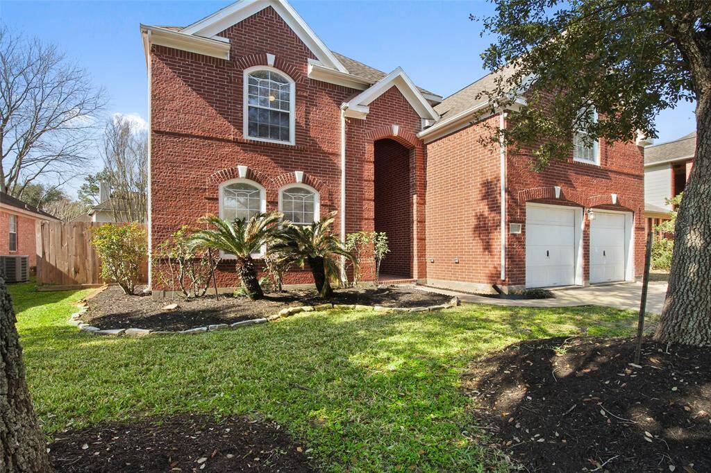 This charming two-story red brick home features a well-kept front yard with mature trees and landscaping. It includes a double garage and classic arched windows, offering great curb appeal in a quiet neighborhood.