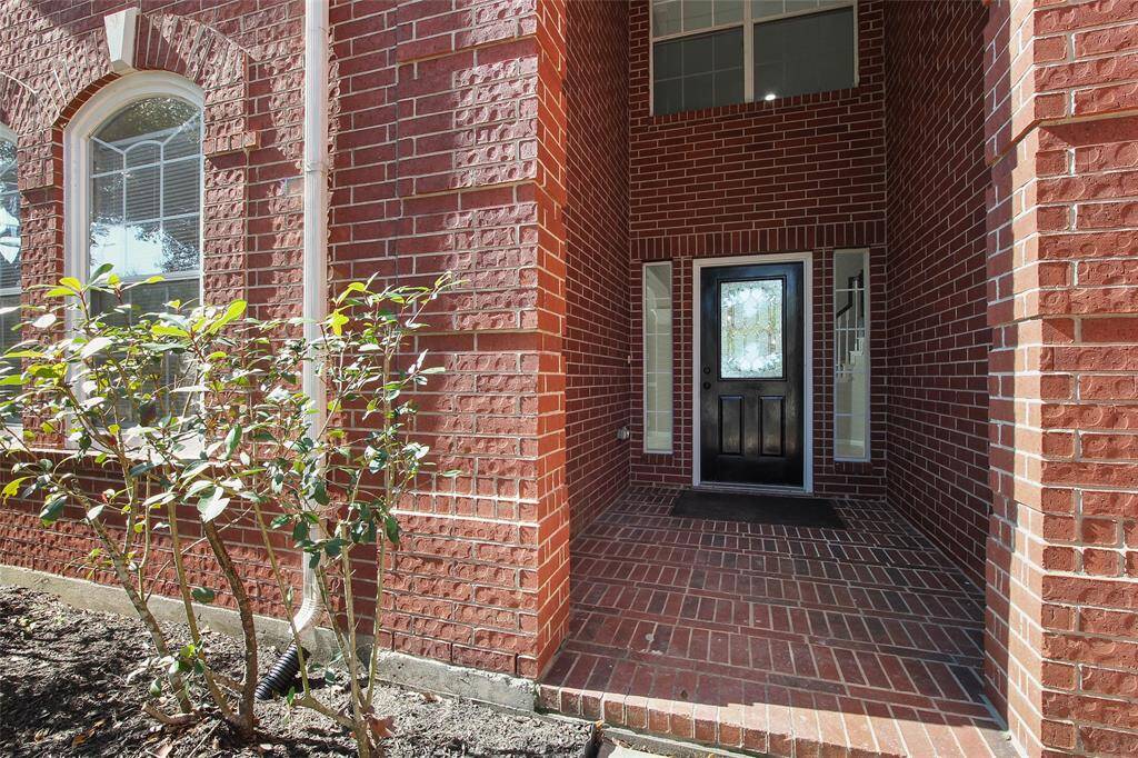 The photo shows a welcoming entrance of a home with a classic brick exterior. It features a covered porch, a black front door with sidelights, and large arched windows, providing an inviting and elegant curb appeal.