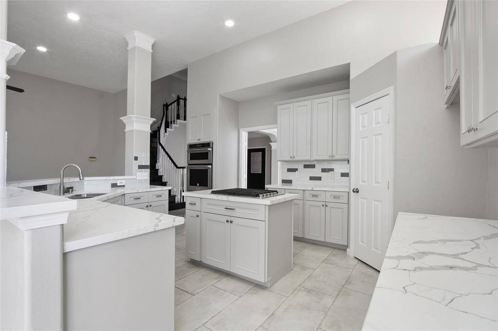 This modern kitchen boasts sleek white cabinetry, a central island with a cooktop, and popular Quartz countertops. The open layout seamlessly connects to the dining area, with natural light enhancing the space's airy feel.