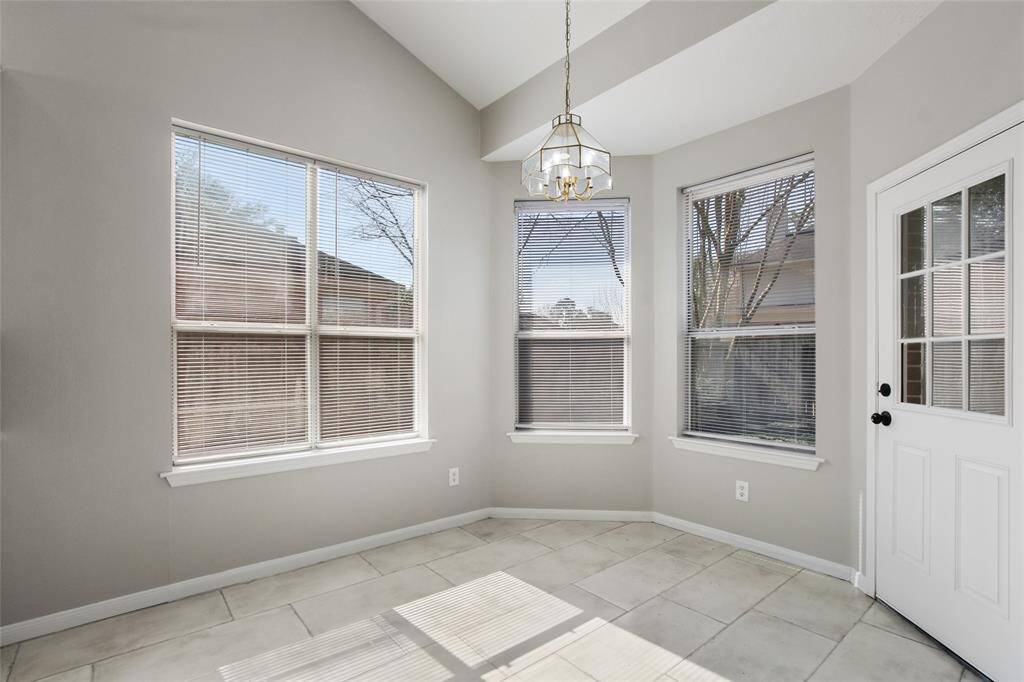 Bright and inviting sunroom featuring large windows with blinds, light gray walls, and a modern chandelier. The tile flooring adds a sleek touch, while the door provides easy outdoor access. Perfect for relaxation or a cozy breakfast nook.