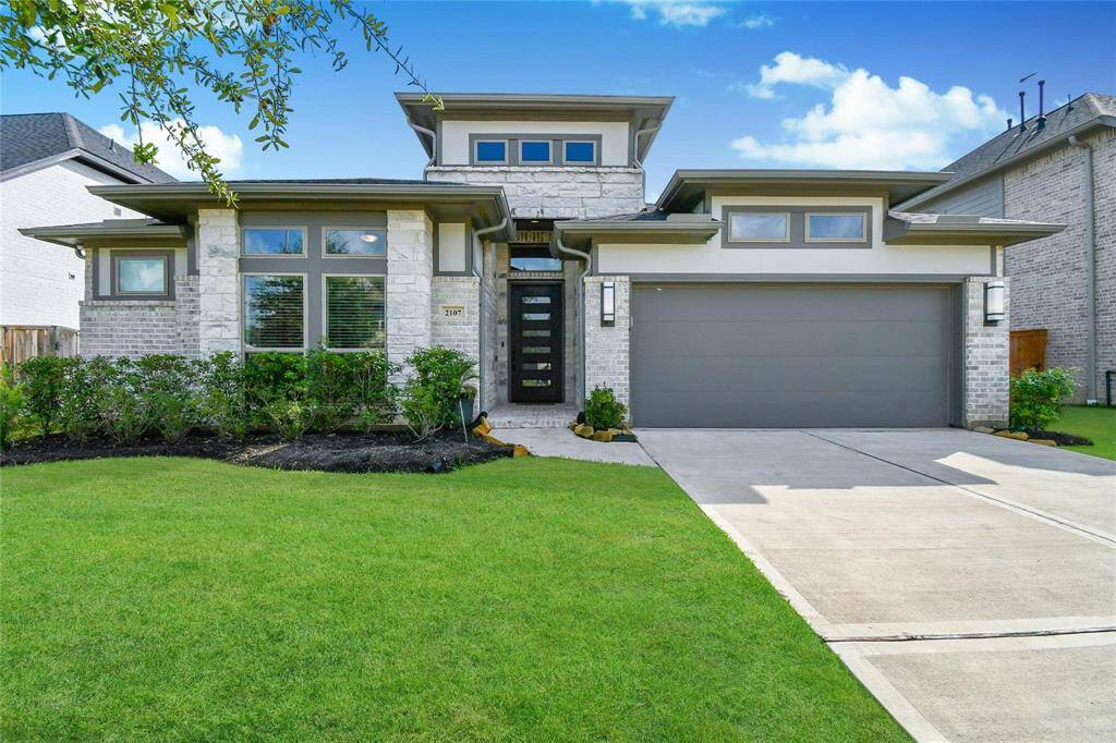This modern home features a sleek design with a two-car garage and a well-maintained front lawn. The stone facade and large windows offer plenty of natural light, enhancing the home's curb appeal.