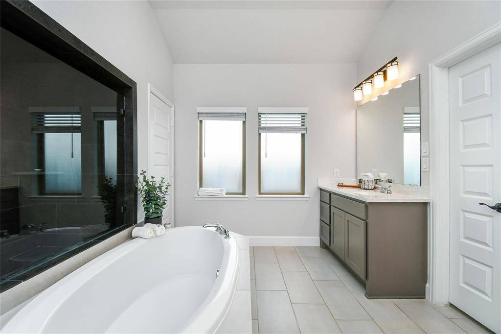 This photo showcases a modern bathroom with a spacious bathtub, large mirror, and a sleek vanity with ample storage. The room is brightened by two frosted windows, and the neutral tones provide a clean, inviting atmosphere.
