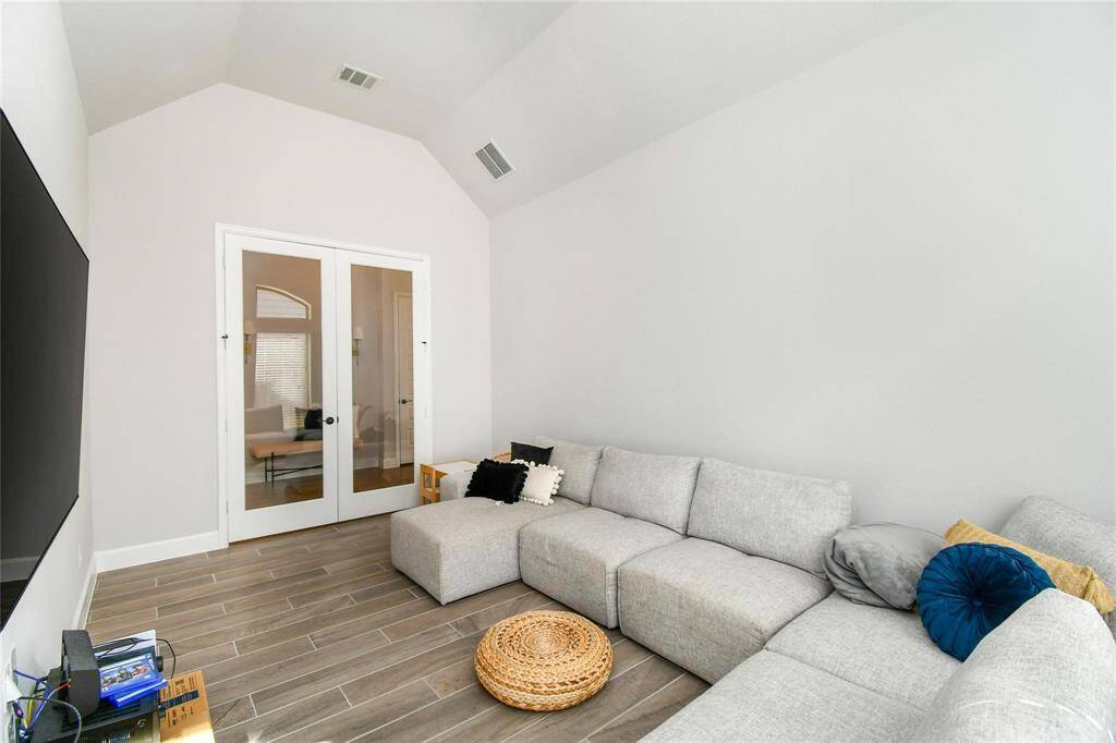 This cozy living area features a large sectional sofa, wood-look tile flooring, and double doors with glass panels, creating a bright and inviting space perfect for relaxation or entertainment.
