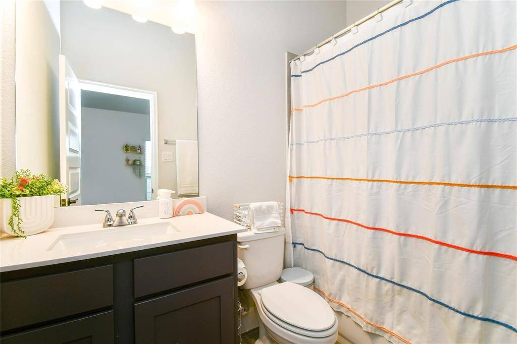 This bathroom features a modern design with a sleek dark vanity, a bright countertop, and a large mirror. It includes a bathtub with a colorful striped curtain and a well-placed toilet. The space is well-lit and inviting.