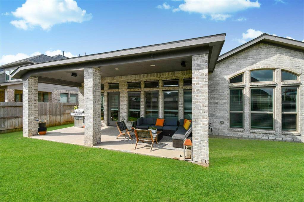 This photo showcases a modern brick home with a spacious covered patio, featuring outdoor seating and a grill. The lush green lawn adds to the inviting outdoor living space, perfect for relaxation and entertaining.