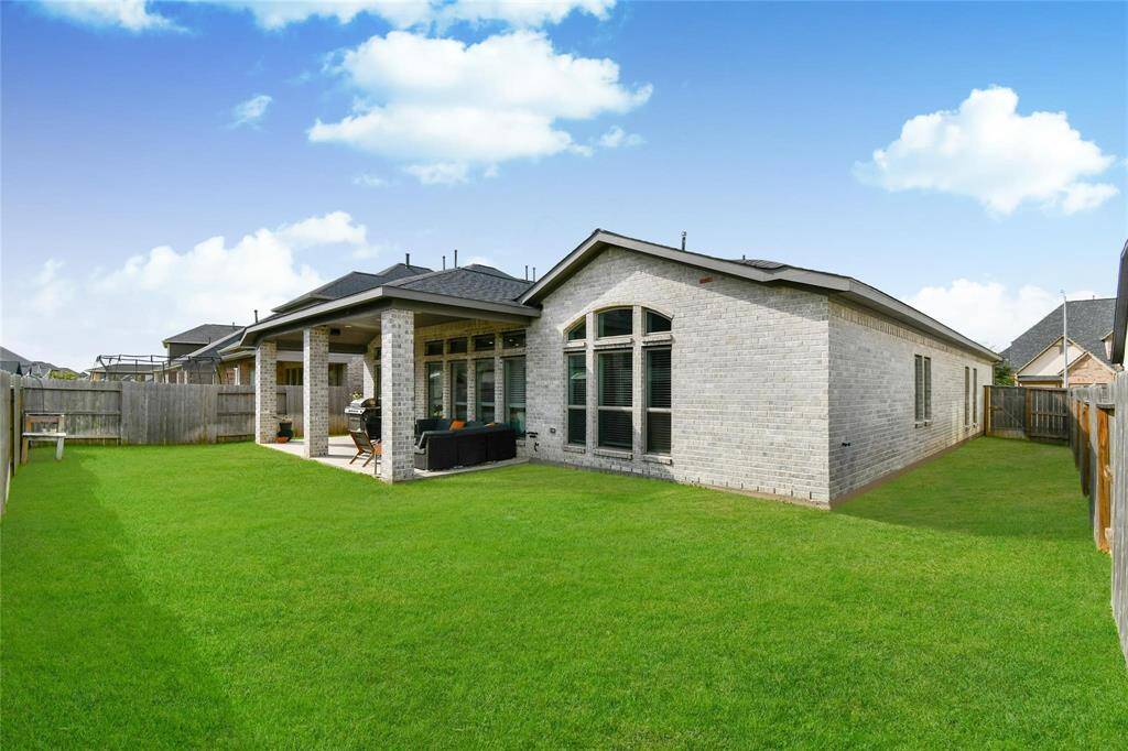 This photo showcases a modern brick home with a spacious, well-maintained backyard. There's a covered patio ideal for outdoor seating or entertaining, and the yard is bordered by a wooden fence, offering privacy.
