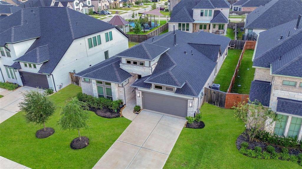 This modern home features a sleek, dark roof and light brick facade, complemented by neat landscaping. It has a spacious driveway leading to a two-car garage. The property is situated in a well-kept neighborhood with similar styled homes, offering a cozy and inviting curb appeal.