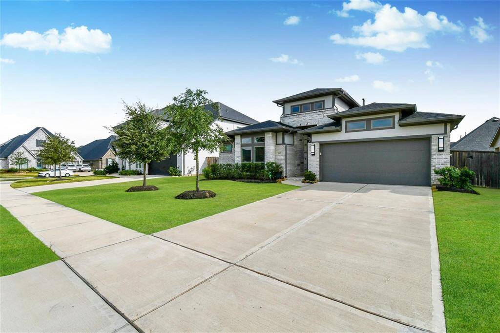 This photo showcases a modern, two-story home with a spacious driveway and attached garage. The exterior features clean lines, a well-maintained lawn, and a few small trees, providing a welcoming curb appeal in a suburban neighborhood.