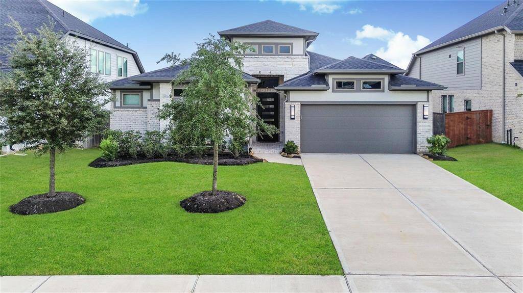 This modern home features a clean, contemporary design with a brick exterior and a two-car garage. It has a well-maintained front lawn with young trees and a neat driveway, offering great curb appeal.