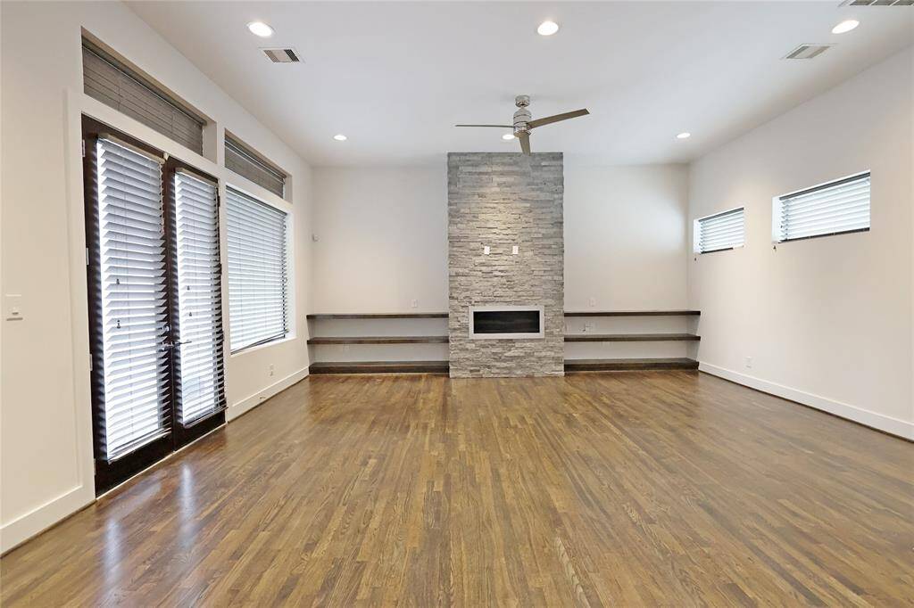 The expansive living room showcases a beautiful stone gas fireplace, custom built-in shelving, recessed lighting, and a stylish modern fan. Double doors lead to the second-floor balcony.