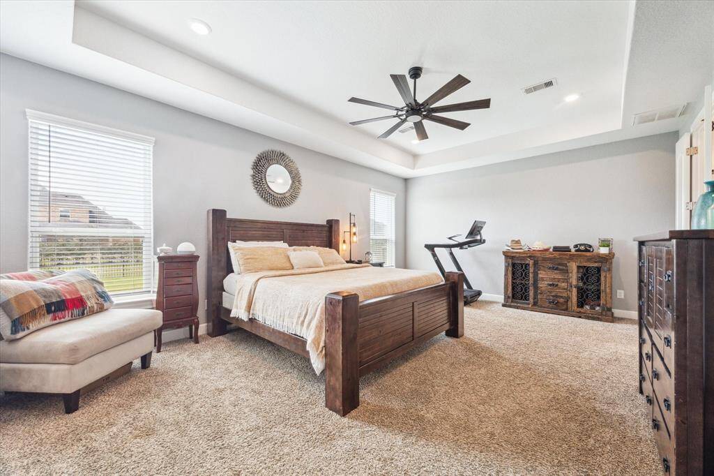 Primary suite features cozy carpet, soothing paint, tray ceiling and large windows.  This room is spacious enough to accommodate oversized furniture and still have room for a seating area.