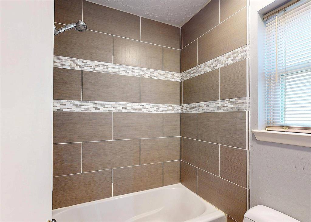 The tub-shower combo of the primary bath with contemporary tile accents and tile that extends to the ceiling.