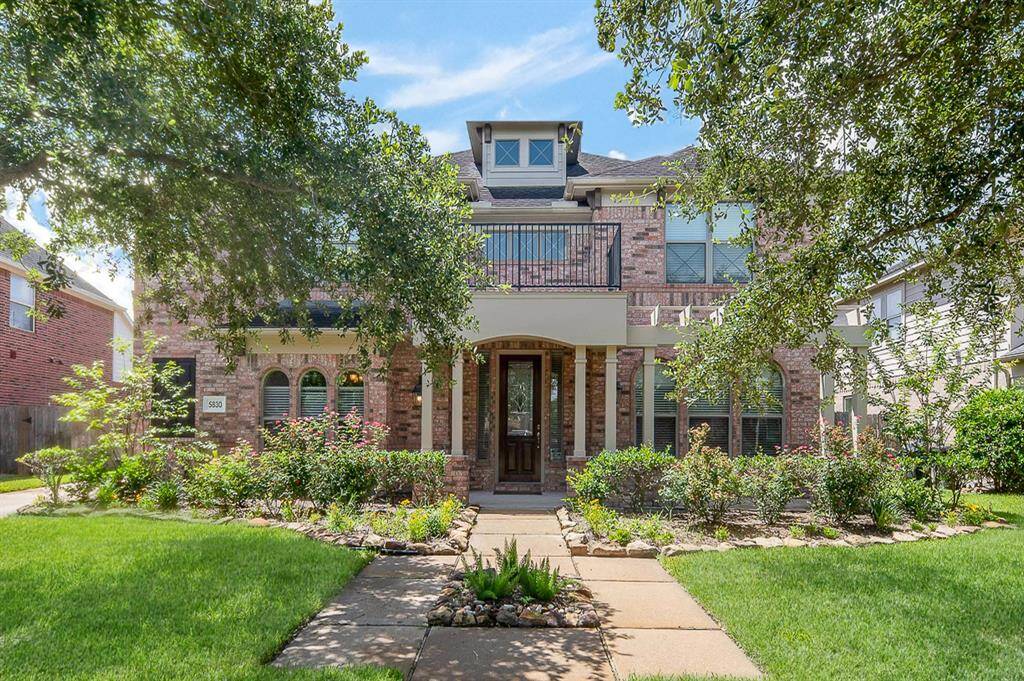 This charming two-story brick home features a welcoming front porch, lush landscaping, and mature trees. The well-maintained yard and classic architectural details create an inviting curb appeal, perfect for a family residence.