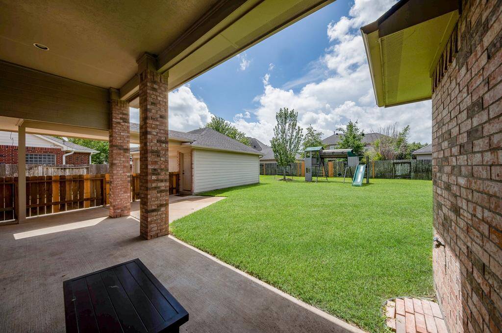This photo showcases a spacious backyard with a covered patio, perfect for outdoor relaxation. The yard features a lush green lawn, a playset, and a storage shed, ideal for family activities and storage. The area is surrounded by a wooden fence, providing privacy.