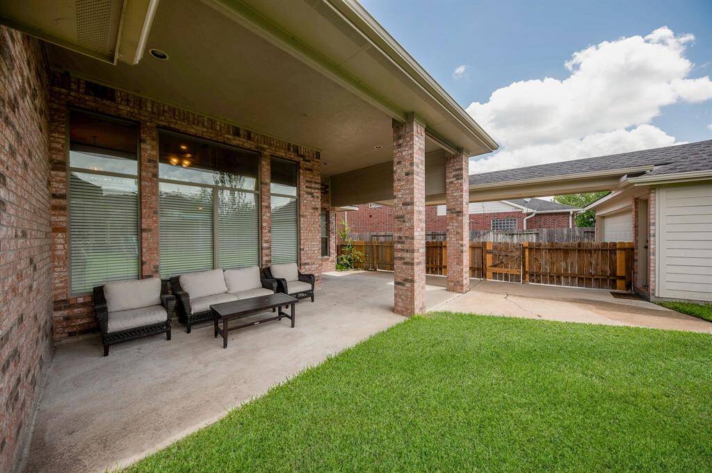 This photo shows a spacious covered patio with comfortable seating, surrounded by a well-maintained lawn. The area is perfect for outdoor relaxation and entertaining, with a view of the fenced backyard and nearby structures.
