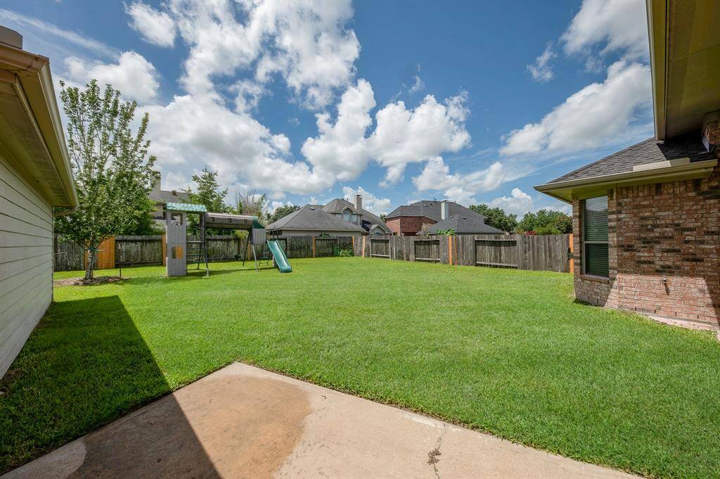 Spacious backyard with a lush green lawn, a playset for kids, and a privacy fence. Ideal for family activities and outdoor relaxation.
