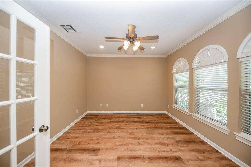 This room off the entryway can could be the office or study and has elegant flooring, neutral walls, and ample natural light from large windows. Features include a ceiling fan and French doors, perfect for a home office or cozy sitting area.