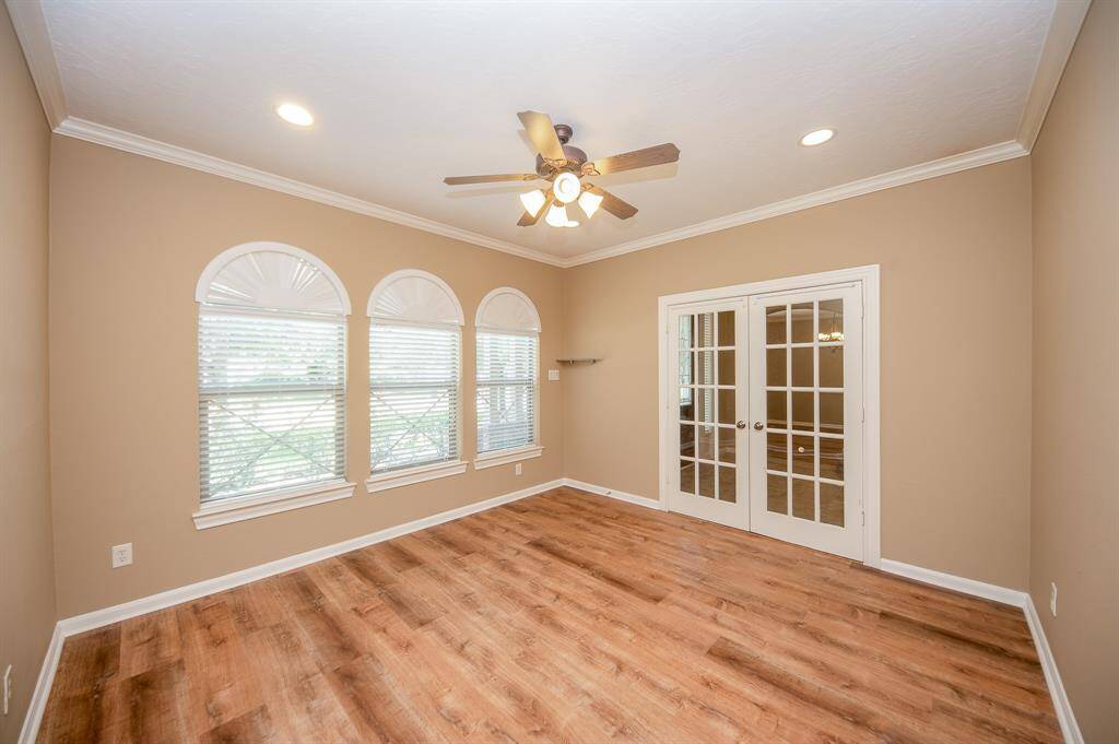 This room features large windows with arched accents, allowing plenty of natural light. It has appealing flooring, neutral walls, and a ceiling fan. French doors lead to an adjoining space, creating an open and inviting atmosphere.