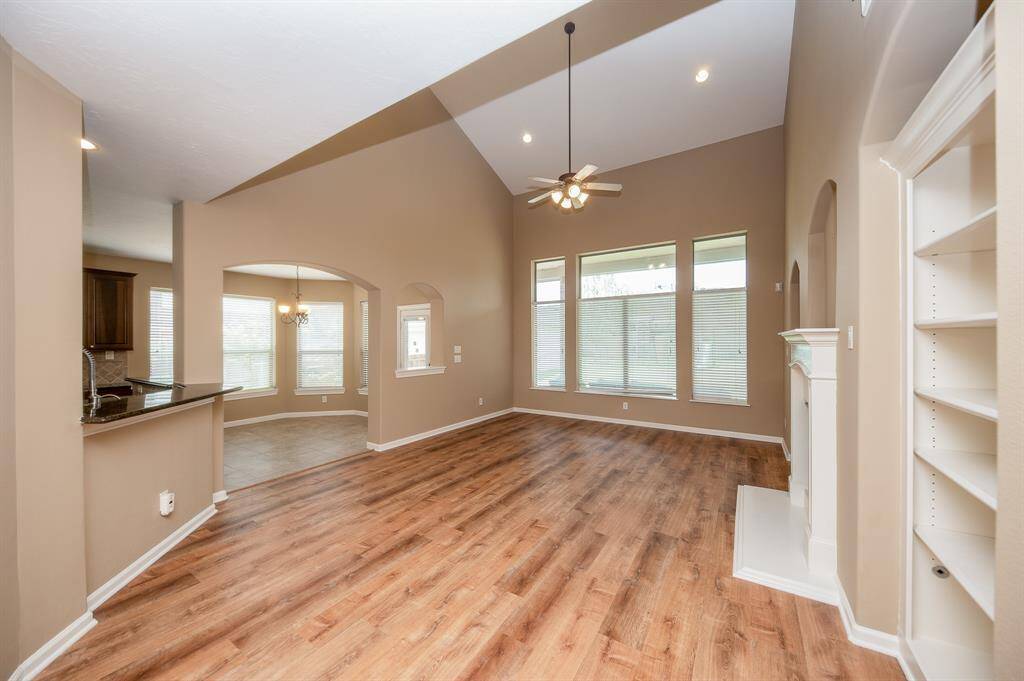 This photo showcases a spacious, open-concept living area with high ceilings and abundant natural light. It features gorgeous floors, built-in shelving, a ceiling fan, and large windows. The space connects seamlessly to a kitchen with a breakfast nook, offering a warm and inviting atmosphere.