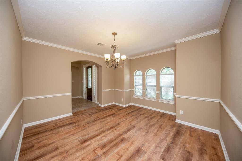 This inviting dining room features elegant flooring, soft beige walls with white trim, and a stylish chandelier. Three arched windows provide natural light, while an arched doorway offers easy access to adjacent spaces.