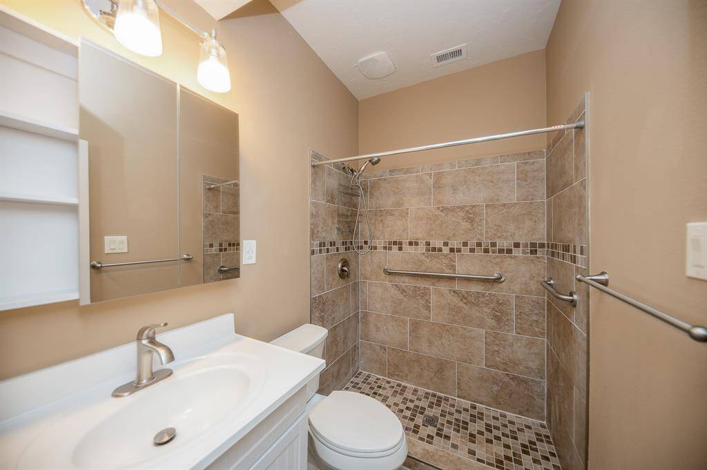 This bathroom features a modern, walk-in shower with tiled walls and floor, a sleek vanity with a mirror, and neutral wall tones for a cozy feel.