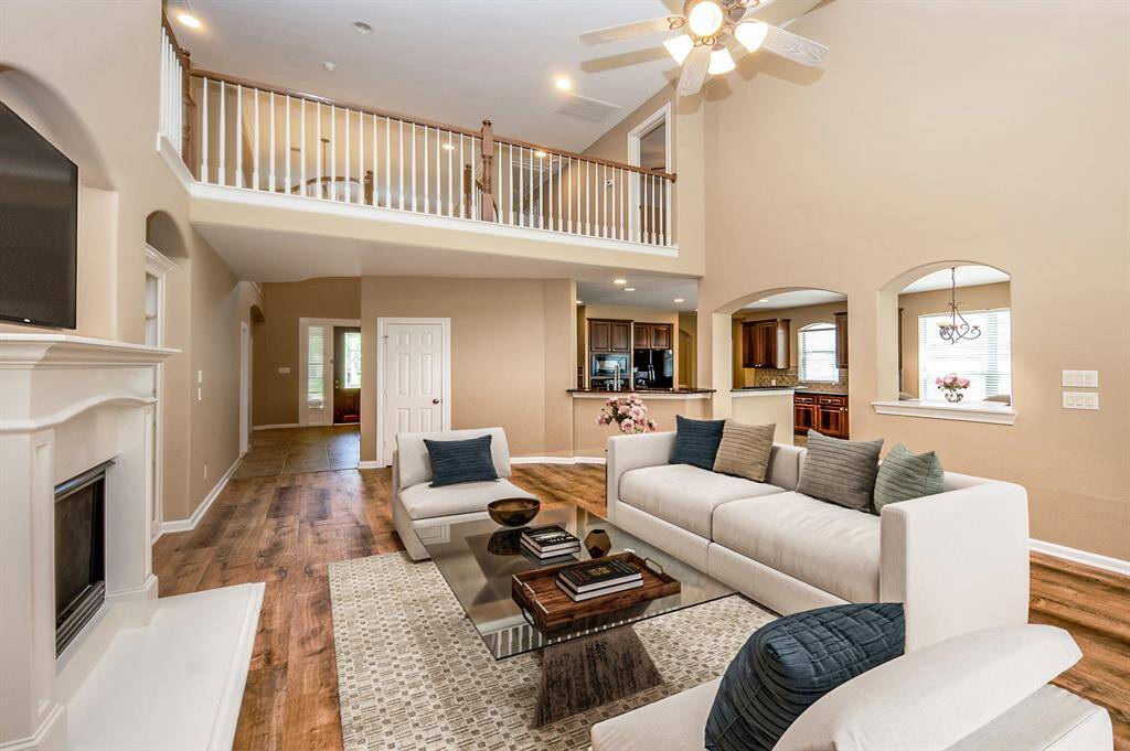 This bright, open-concept living area features high ceilings, a cozy fireplace, and elegant flooring. The space seamlessly connects to a modern kitchen with warm cabinetry and a breakfast nook, creating a welcoming atmosphere for gatherings. Image is Virtually Staged.