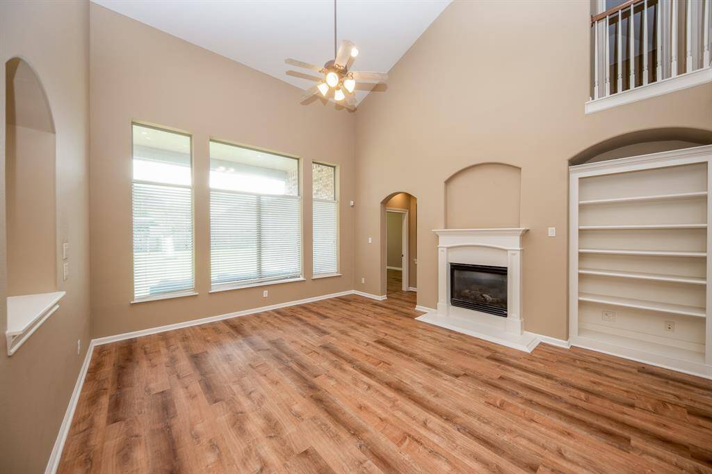 This spacious living room features high ceilings, large windows with ample natural light, a cozy fireplace, and built-in shelving. The warm colore d flooring and neutral wall colors create an inviting atmosphere.