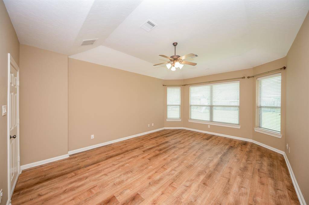 Spacious primary bedroom with appealing flooring, neutral walls, and a ceiling fan. Large windows provide ample natural light, creating an inviting atmosphere. Ideal for a living area or master bedroom.