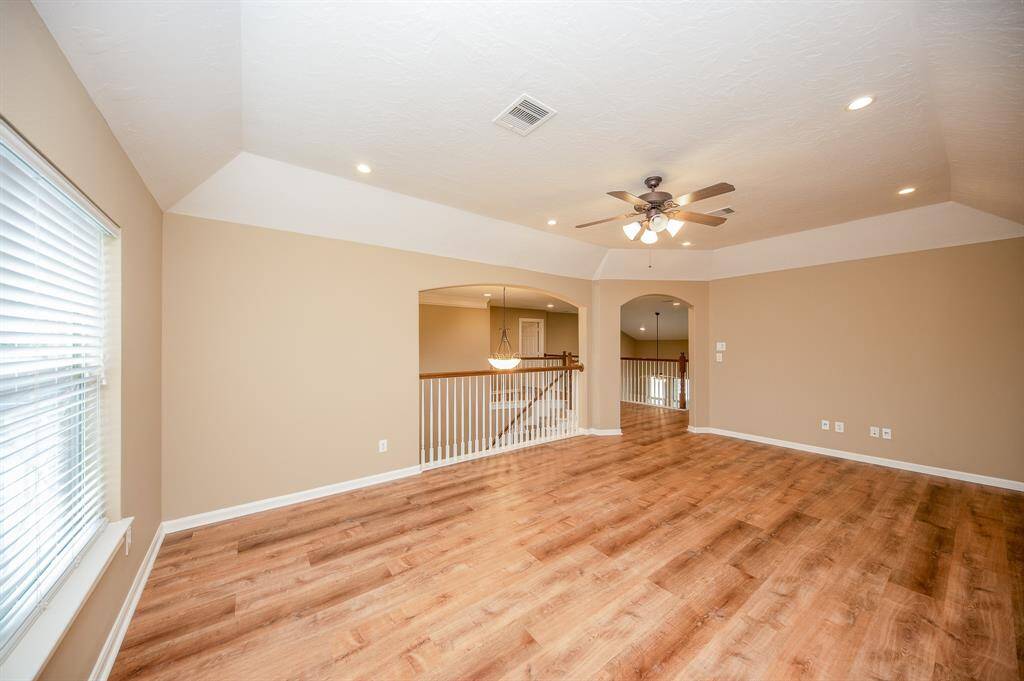 This spacious, open-concept game room features warm elegant flooring, a ceiling fan, and recessed lighting. It offers plenty of natural light through large windows and has an inviting view of the staircase and adjacent areas. Perfect for comfortable living and entertaining.