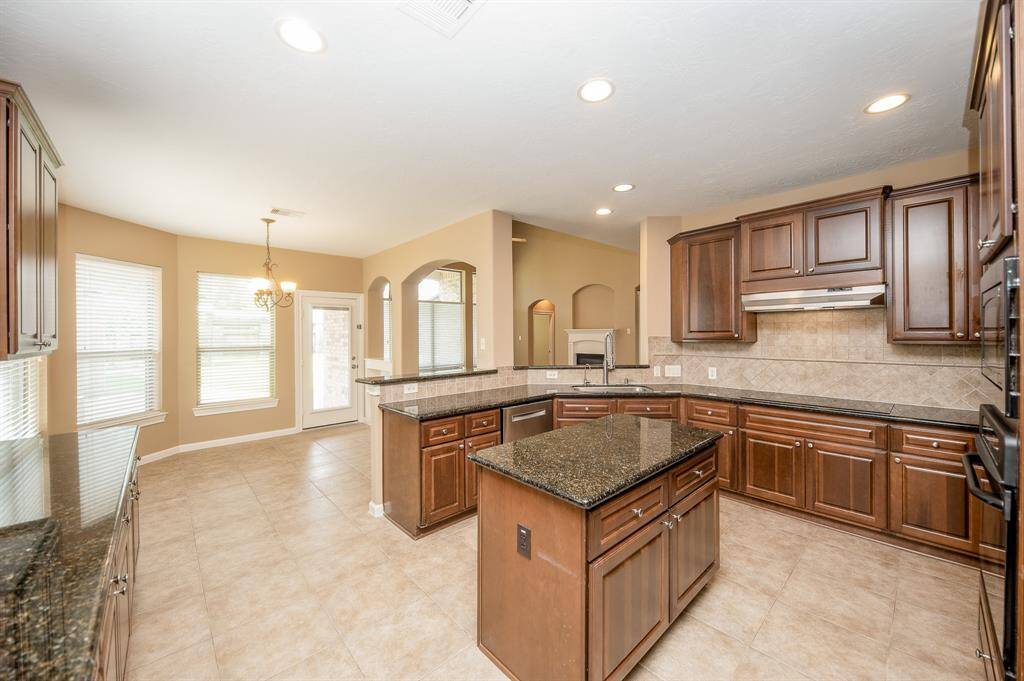 Spacious kitchen with dark wood cabinetry, granite countertops, and a central island. It features tile flooring, recessed lighting, and a cozy breakfast nook with large windows and a chandelier. The layout is open and inviting, ideal for cooking and entertaining.