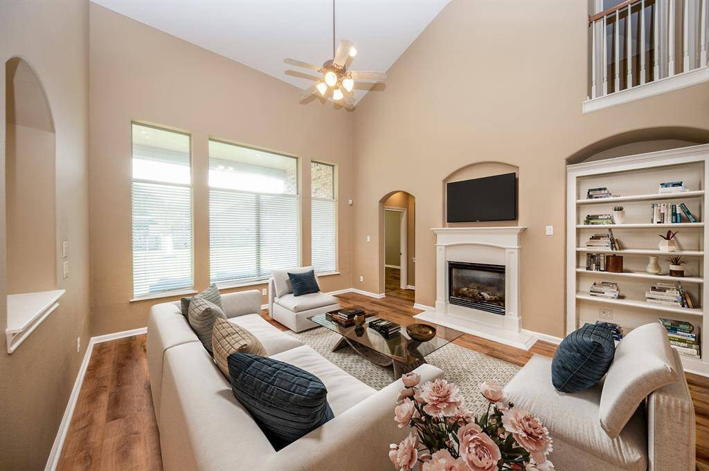 This spacious living room features high ceilings, a cozy fireplace, and large windows for natural light. It includes a built-in bookshelf, modern styled flooring, and neutral tones, creating an inviting and comfortable atmosphere. Image is Virtually Staged.