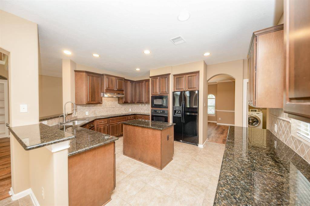 This kitchen features modern appliances, dark wood cabinetry, and granite countertops. It includes an island for extra workspace and a spacious layout, ideal for cooking and entertaining. The tile flooring and recessed lighting add a warm, inviting touch.