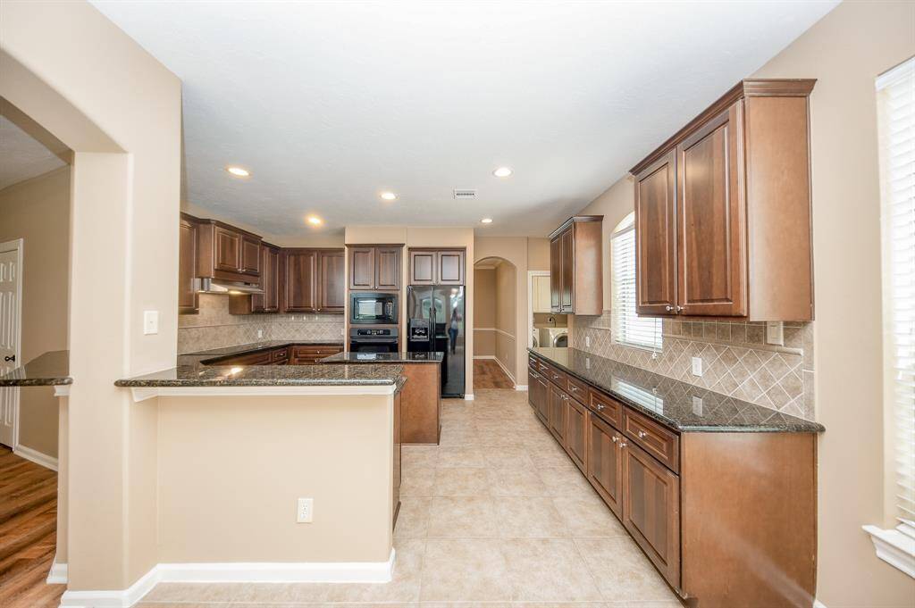 This spacious kitchen features elegant dark wood cabinetry, granite countertops, and modern appliances. The open layout includes ample counter space and a breakfast bar, complemented by natural light from large windows.