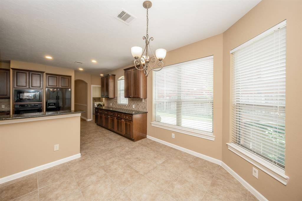 This photo showcases a bright, open kitchen and dining area with large windows, neutral tile flooring, and dark wood cabinetry. The space includes a modern chandelier and a spacious counter area, ideal for gatherings.