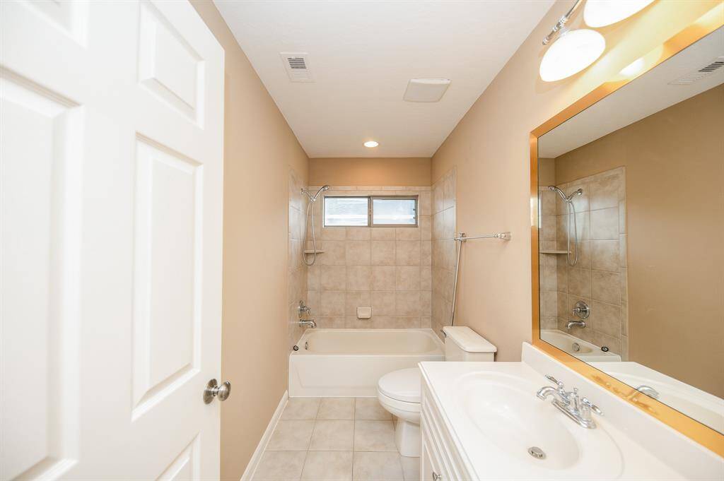 This bathroom features a clean, neutral design with a tiled shower/bathtub combo, a single vanity with a large mirror, and overhead lighting. The space is well-lit, providing a fresh and inviting atmosphere.