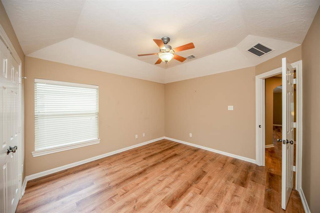 This room features warm beige walls and complimenting flooring, creating a cozy atmosphere. It includes a ceiling fan with light, a large window for natural light. Ideal for a cozy bedroom or office space.