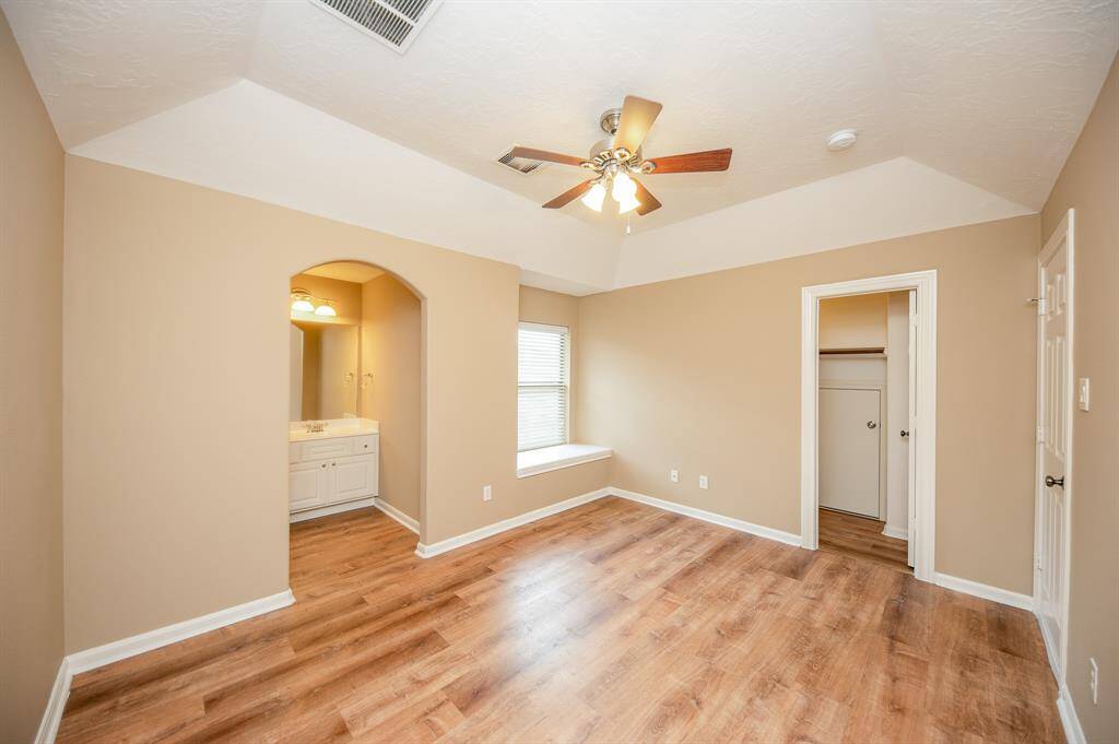 This bright bedroom features a vaulted ceiling, wood flooring, and a ceiling fan. There's a cozy nook with a window seat, an en-suite bathroom with a vanity, and a spacious closet.