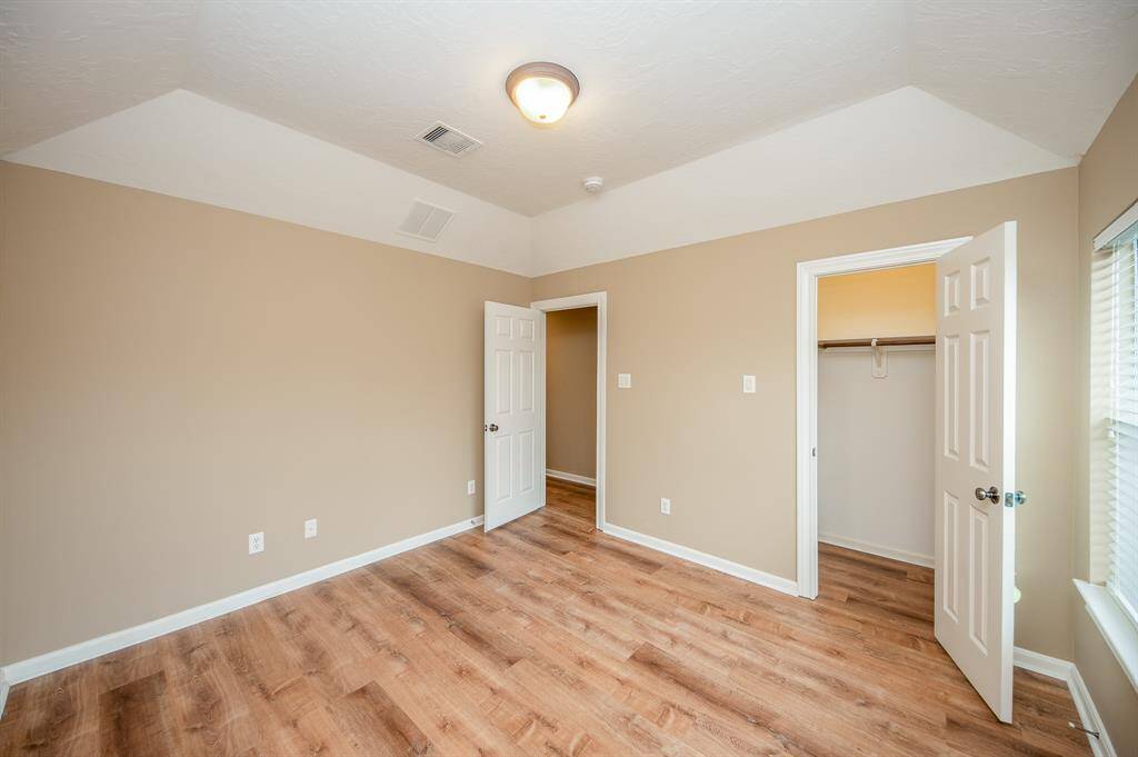 This is a bright, spacious bedroom with neutral walls and wood flooring. It features a ceiling light and two doors, one leading to a closet. Natural light enters through a window, creating a welcoming atmosphere.